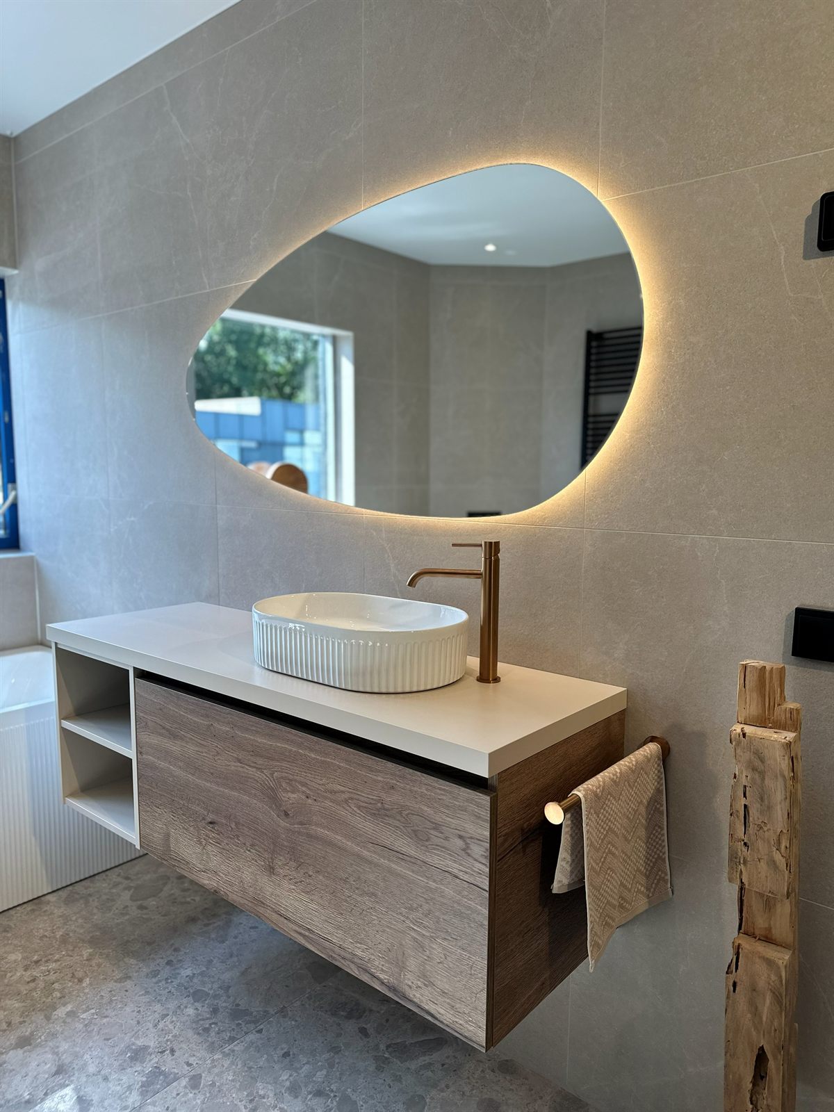 Badkamer met zwevend wastafelmeubel, ovale verlichte spiegel en beige tegelwerk in de showroom van Baderie Almere